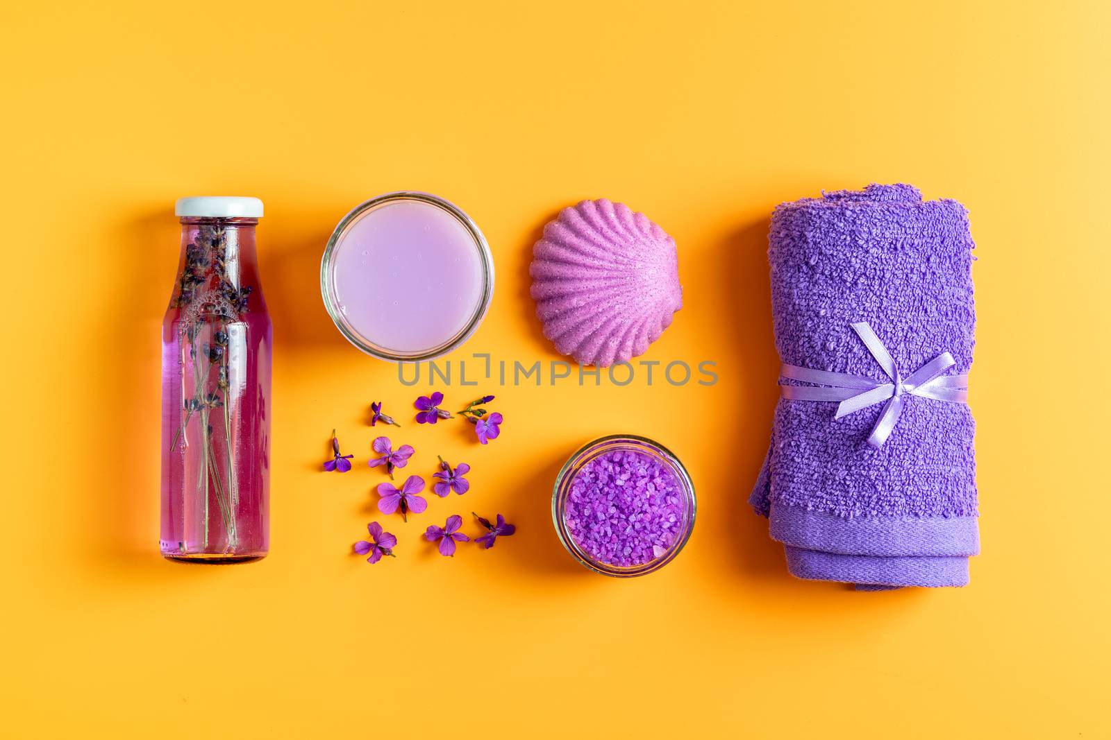 Spa products. Lavender bath salts, viola flowers, soap, cosmetic cream and towel. Violet purple concept. Flat lay on yellow background, top view.