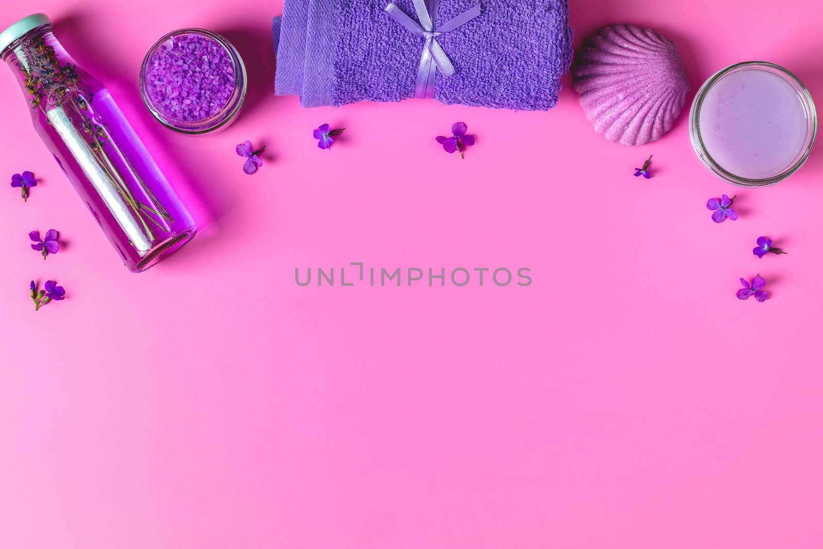 Spa products. Lavender bath salts, viola flowers, soap, cosmetic cream and towel. Violet purple concept. Flat lay on pink background, top view.