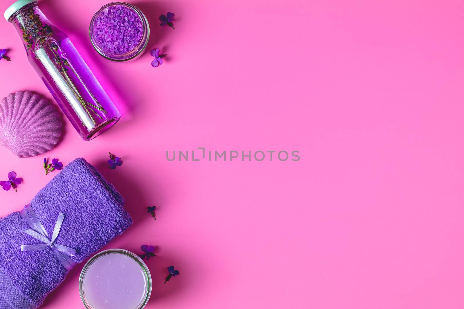 Spa products. Lavender bath salts, viola flowers, soap, cosmetic cream and towel. Violet purple concept. Flat lay on pink background, top view.