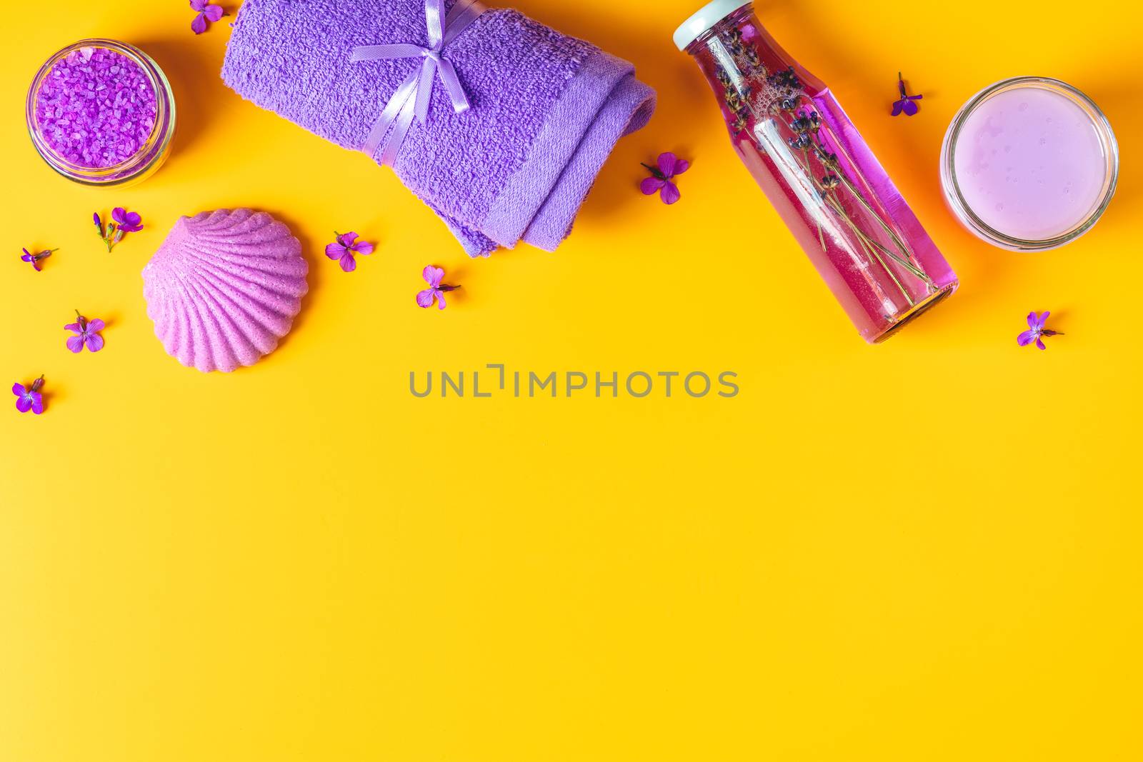 Spa products. Lavender bath salts, viola flowers, soap, cosmetic cream and towel. Violet purple concept. Flat lay on yellow background, top view.