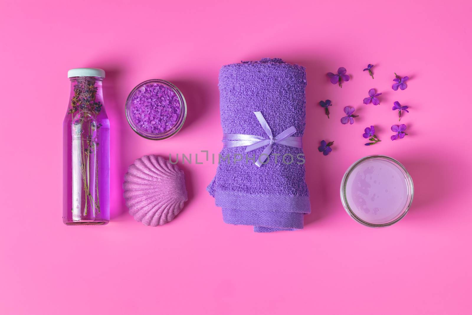 Spa products. Lavender bath salts, viola flowers, soap, cosmetic cream and towel. Violet purple concept. Flat lay on pink background, top view.