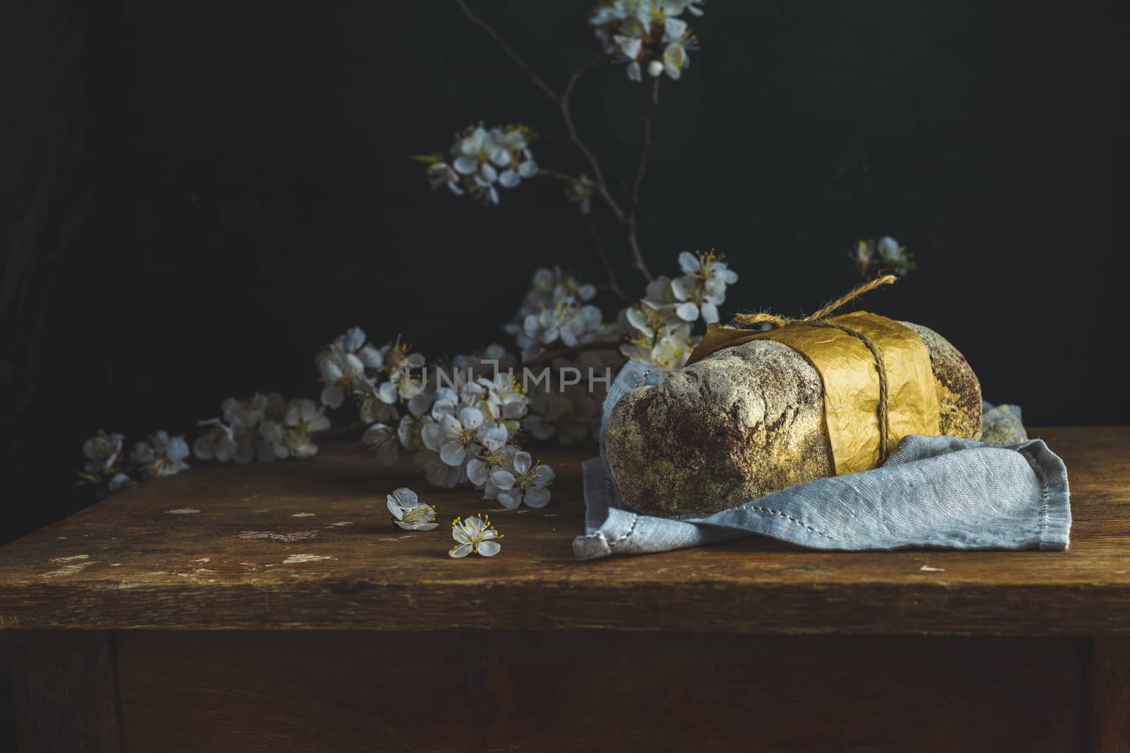 Freshly baked rye handmade breads on old wooden table with linen napkin and apricot tree blossom branch. Dark rustic style. Photo styling of paintings by Flemish painters