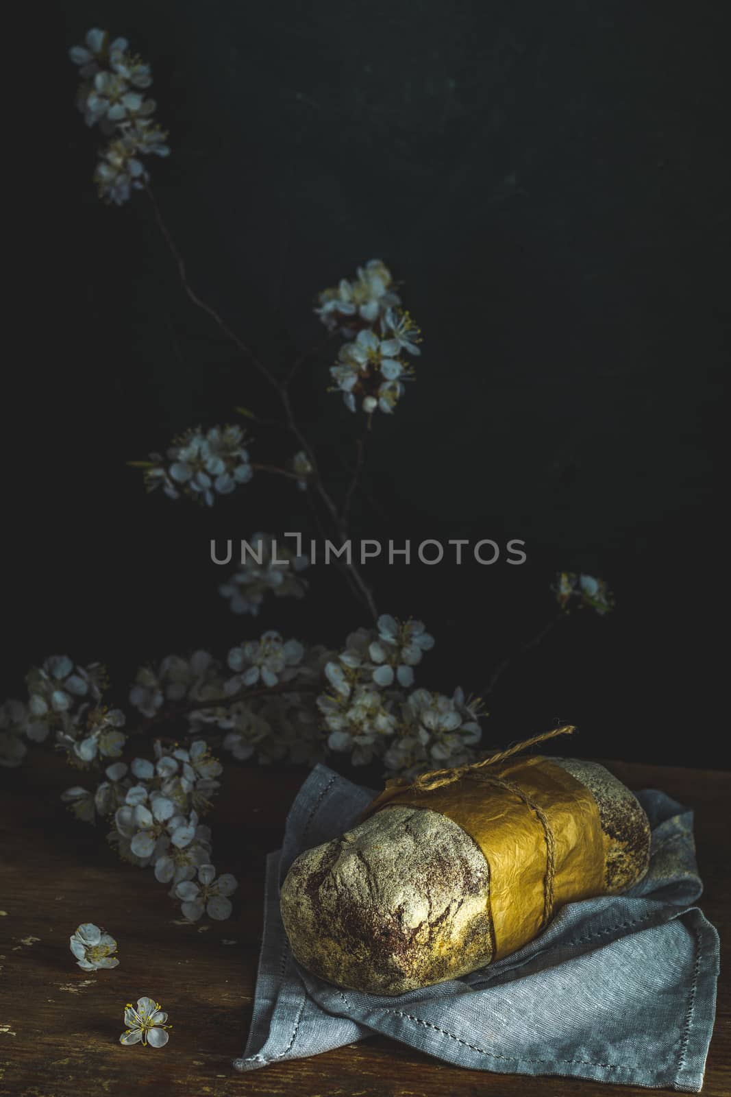 Freshly baked rye handmade breads on old wooden table with linen napkin and apricot tree blossom branch. Dark rustic style. Photo styling of paintings by Flemish painters