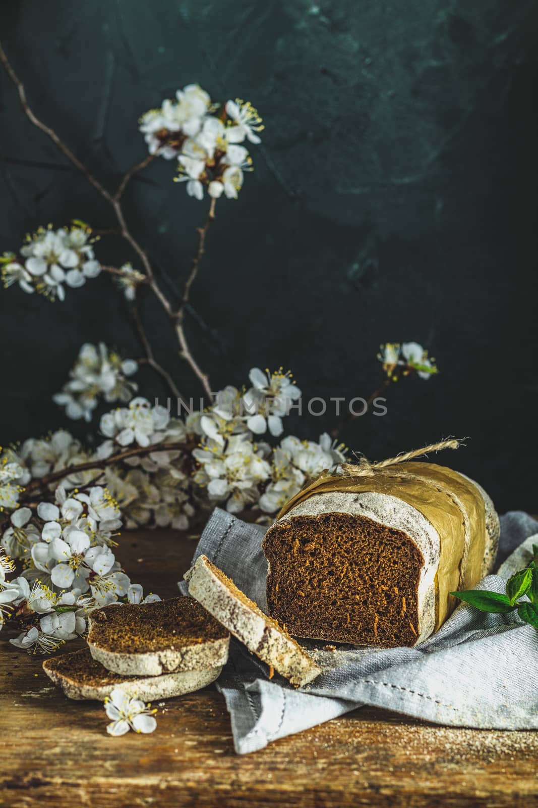 Freshly baked rye handmade breads on old wooden table with linen napkin and apricot tree blossom branch. Dark rustic style. Photo styling of paintings by Flemish painters