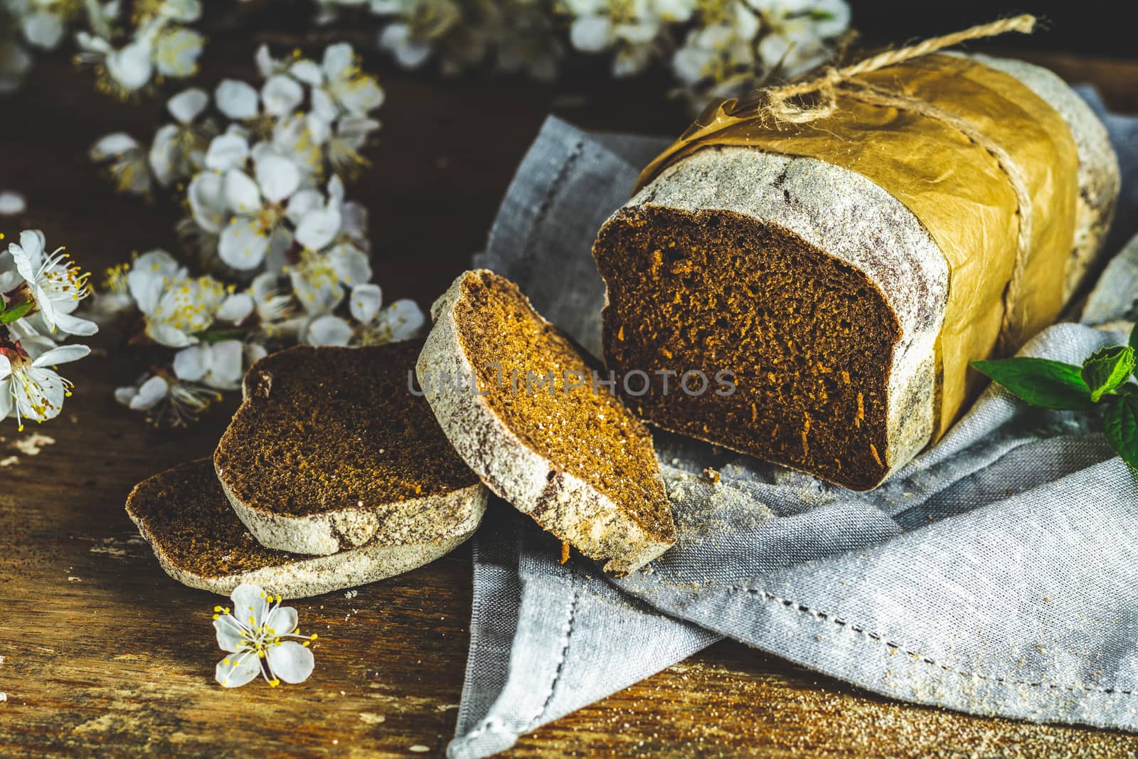 Sliced freshly baked rye handmade breads on old wooden table with linen napkin and apricot tree blossom branch. Dark rustic style.