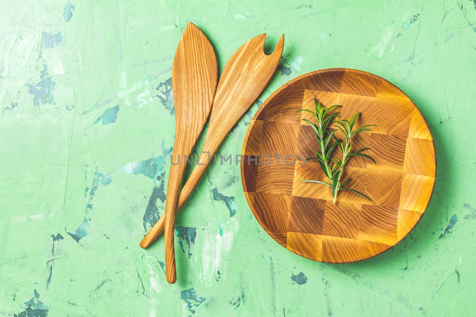 Wooden spoons for salad and wooden plate over green concrete texture background, healthy food concept, top view, copy space for you text.