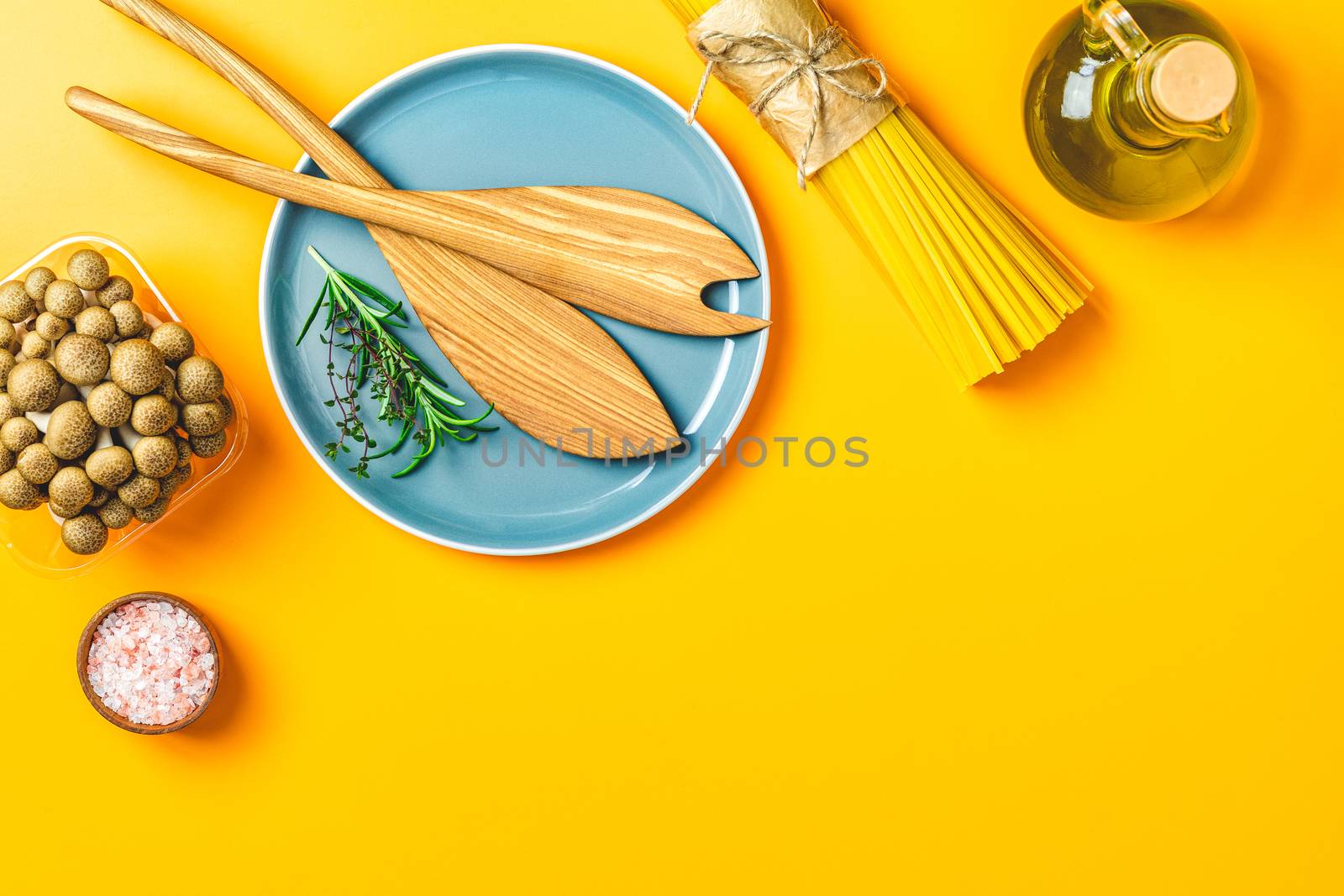 Spaghetti, shimeji mushroom, olive oil,  pink salt, empty ceramic bowl, wooden spoons for salad over yellow background. Top view, flat lay, healthy food concept, copy space for you text.