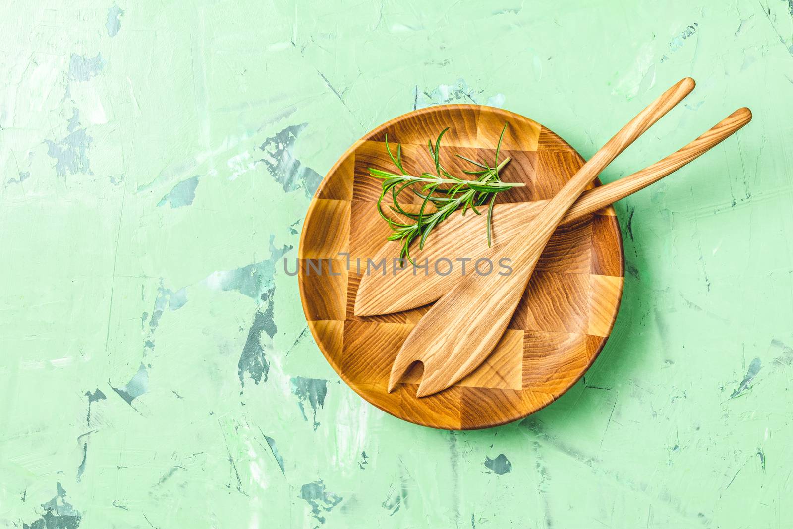 Wooden spoons for salad in wooden plate over green concrete texture background, healthy food concept, top view, copy space for you text.