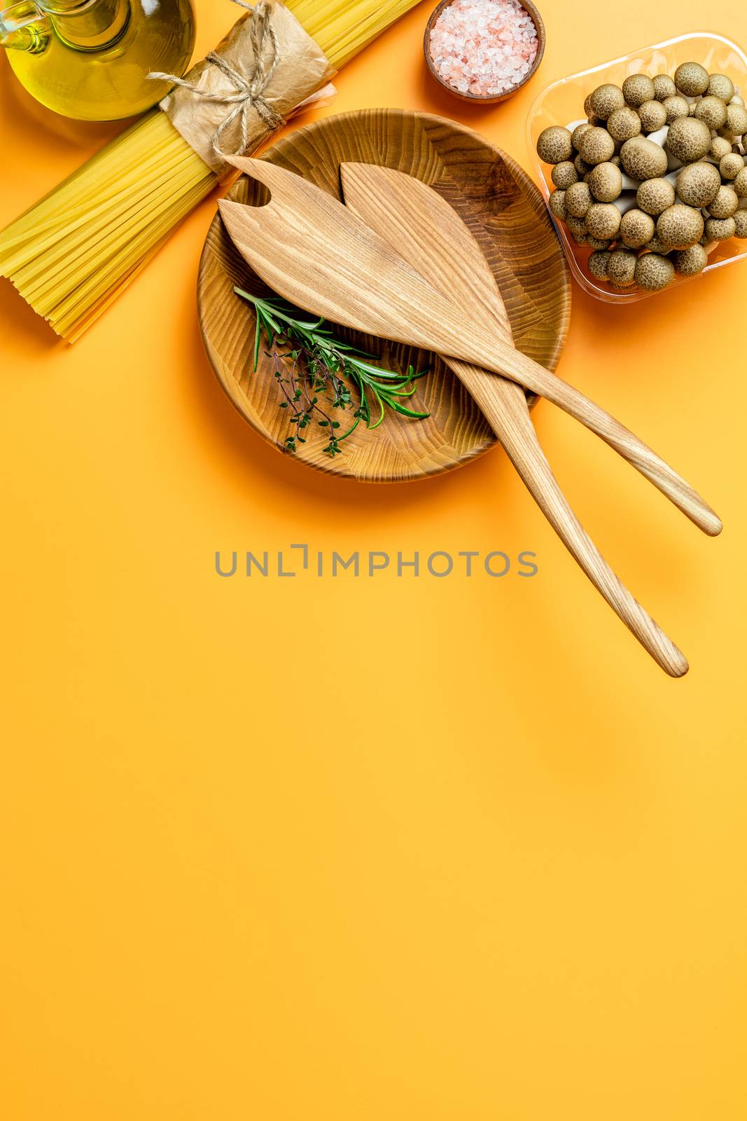 Spaghetti, shimeji mushroom, olive oil,  pink salt, empty wooden bowl, wooden spoons for salad over yellow background. Top view, flat lay, healthy food concept, copy space for you text.