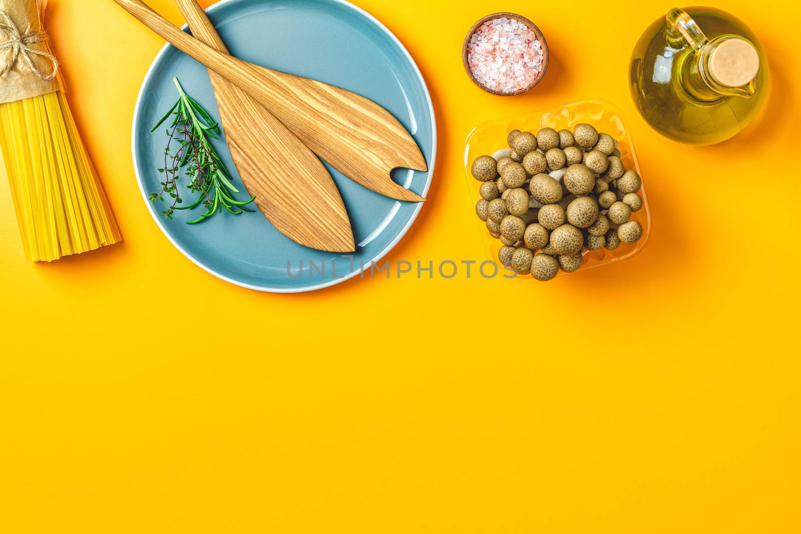 Spaghetti, shimeji mushroom, olive oil,  pink salt, empty ceramic bowl, wooden spoons for salad over yellow background. Top view, flat lay, healthy food concept, copy space for you text.