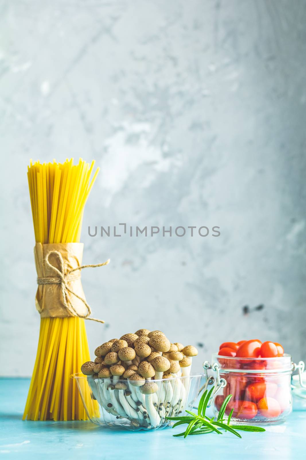 Spaghetti, shimeji mushroom, olive oil,  pink salt, empty ceramic bowl, wooden spoons for salad over blue concrete background. Healthy food concept, copy space for you text.