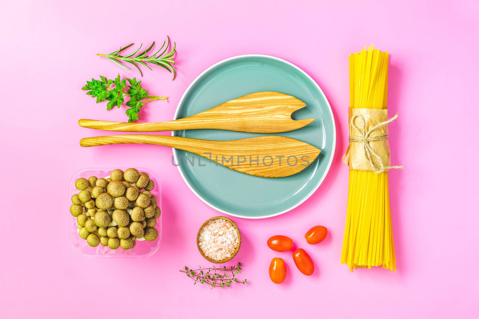 Spaghetti, shimeji mushroom, olive oil,  pink salt, empty ceramic bowl, wooden spoons for salad over pink background. Top view, flat lay, healthy food concept, copy space for you text.
