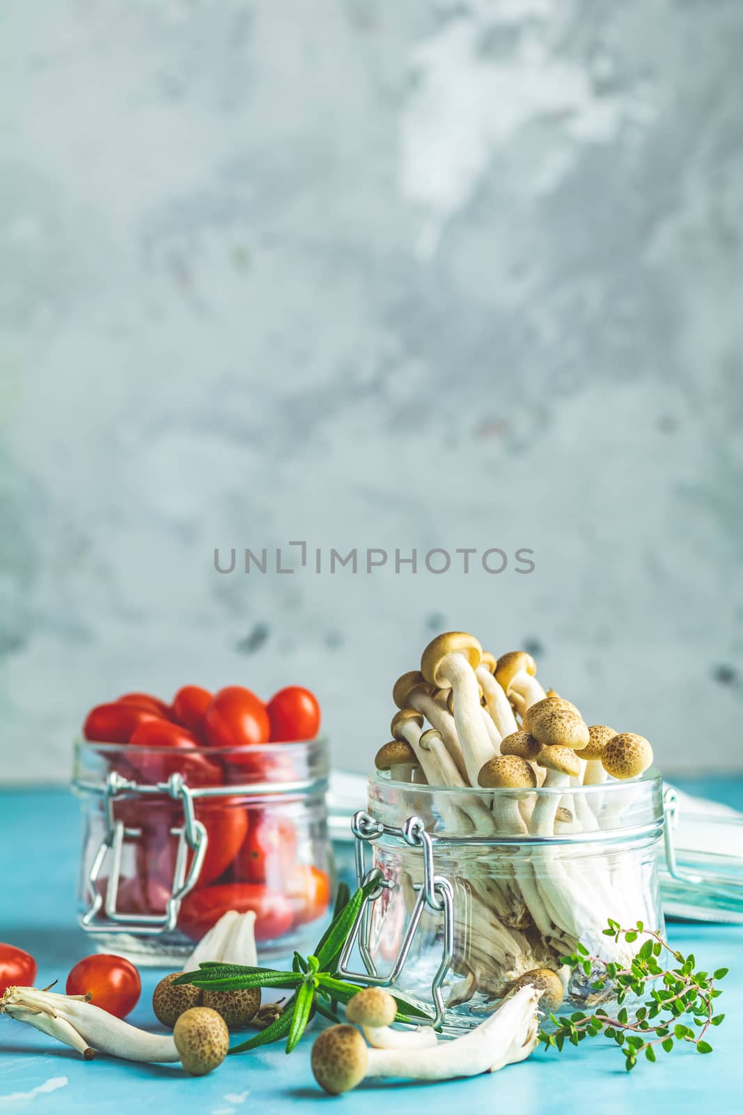 Buna Shimeji - edible mushroom from East Asia. Good food for good health. Clump of shimeji mushroom and cherry tomatoes in jars on blue concrete surface background