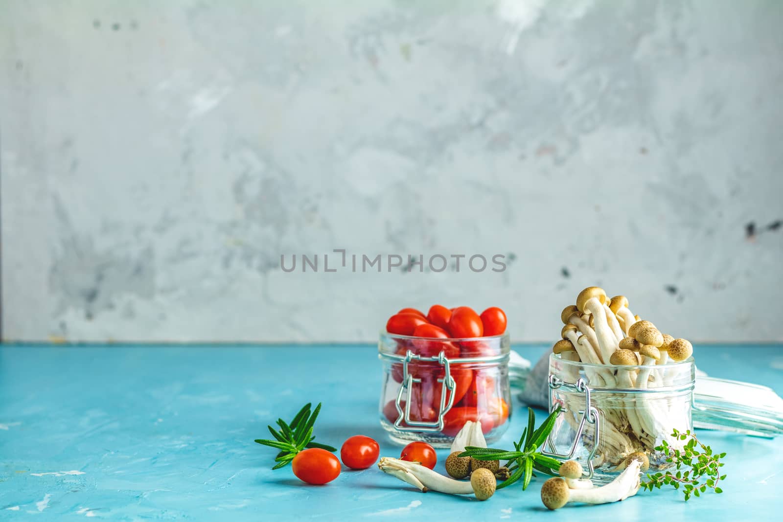 Buna Shimeji - edible mushroom from East Asia. Good food for good health. Clump of shimeji mushroom and cherry tomatoes in jars on blue concrete surface background