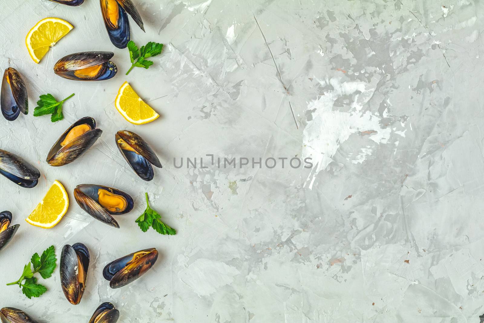 Seafood mussels with lemon and parsley on light gray concrete table surface, top view, copy space for you text