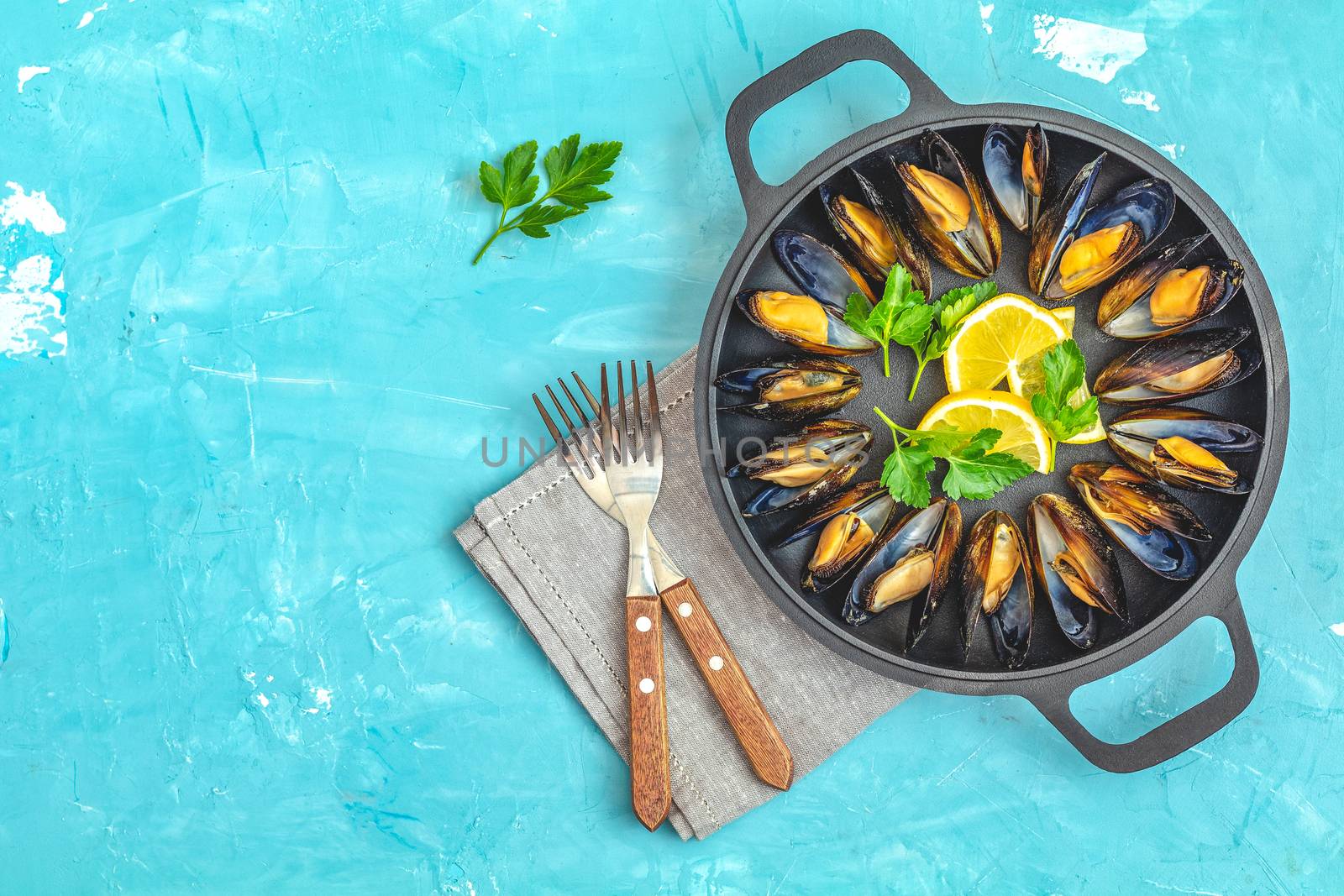 Seafood mussels with lemon and parsley in black metal pan on blue concrete table surface, top view, copy space for you text