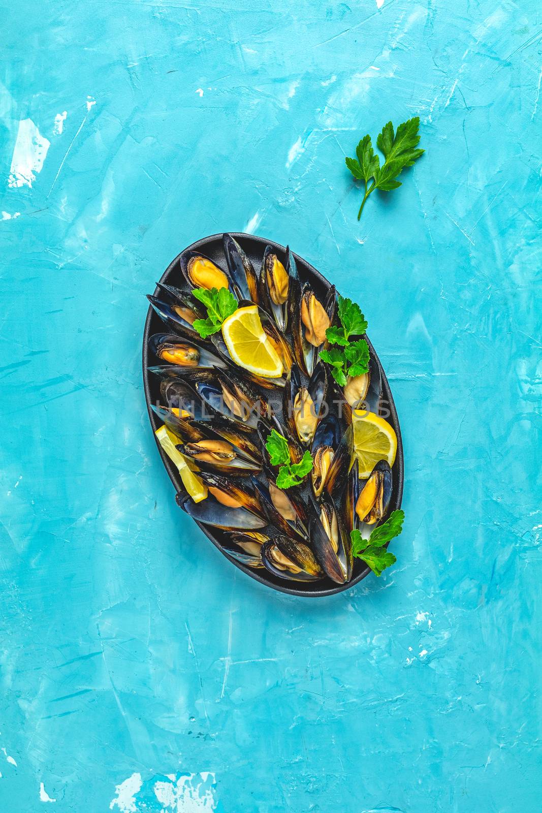 Seafood mussels with lemon and parsley in black metal plate by ArtSvitlyna