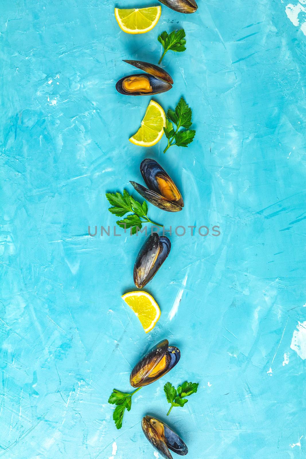 Seafood mussels with lemon and parsley on light blue concrete table surface, top view, copy space for you text