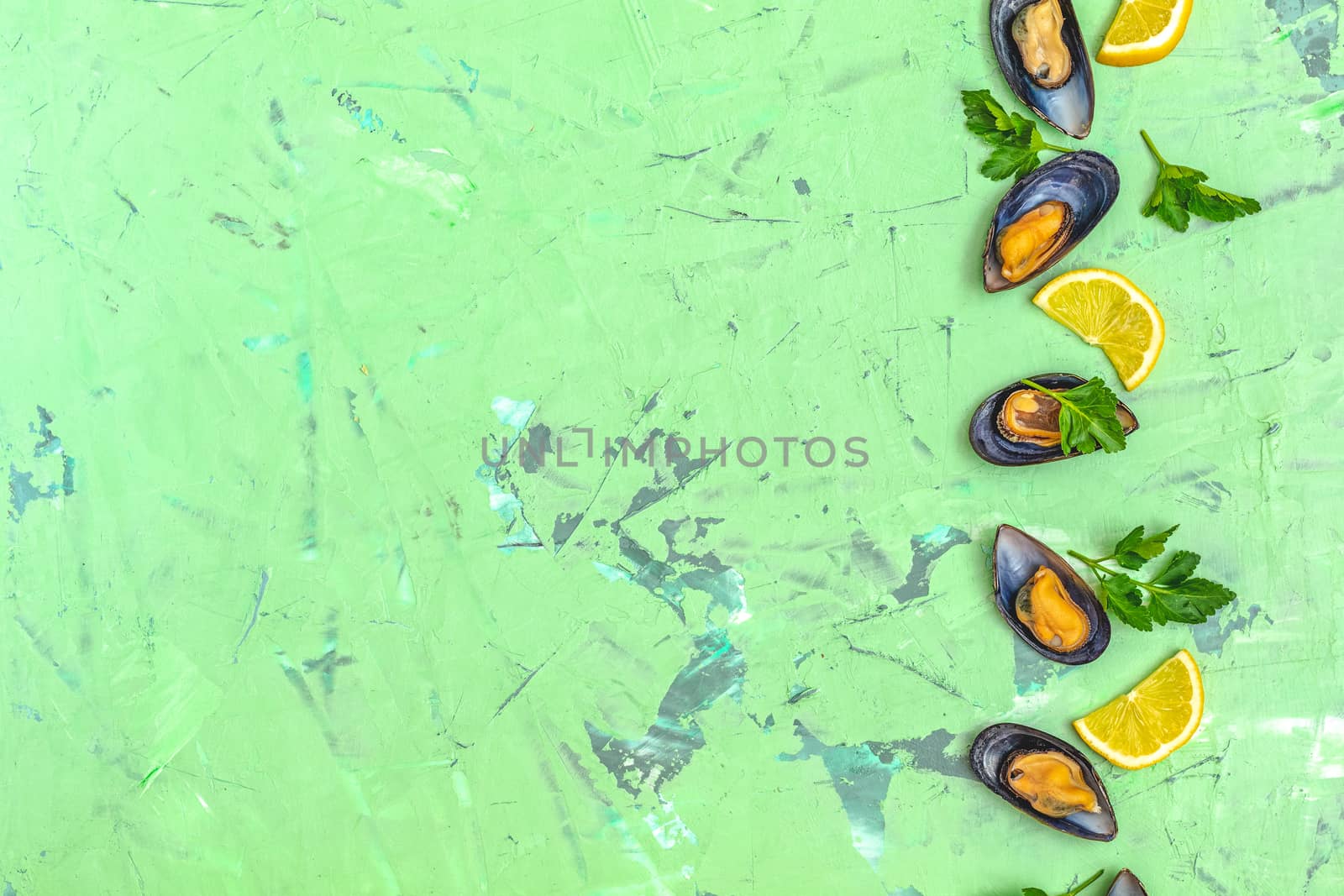 Seafood mussels with lemon and parsley on green concrete table surface, top view, copy space for you text