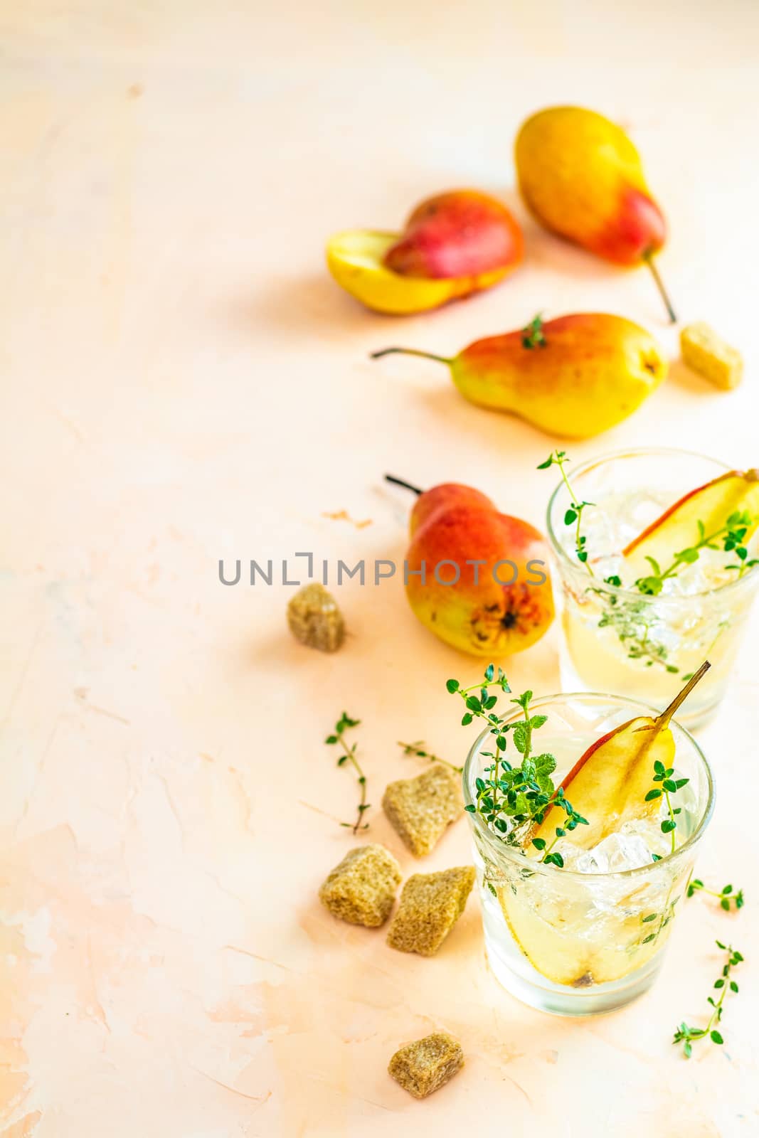 Cold pear white tea with thyme on the pink concrete table background. Festive summer drinks, pear thyme cocktail. Selective focus, space for text