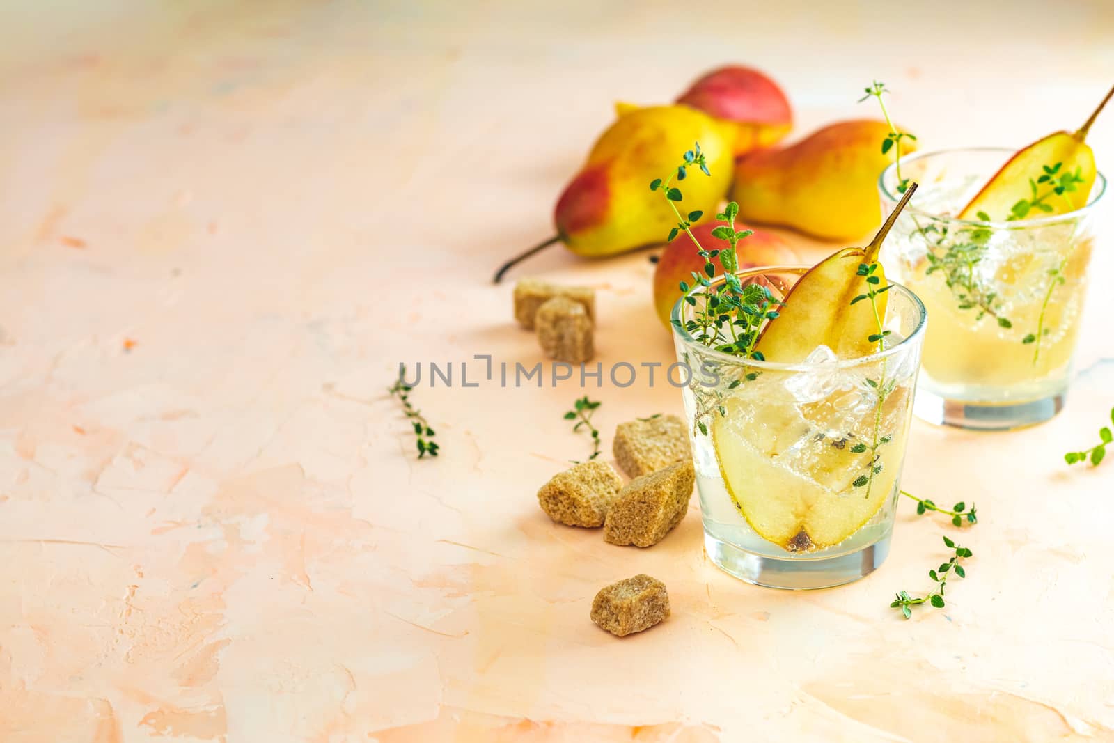 Cold pear white tea with thyme on the pink concrete table background. Festive summer drinks, pear thyme cocktail. Selective focus, space for text
