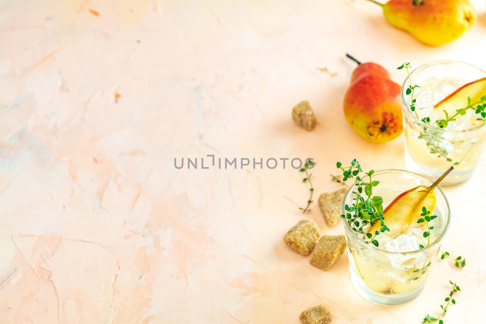 Cold pear white tea with thyme on the pink concrete table background. Festive summer drinks, pear thyme cocktail. Selective focus, space for text