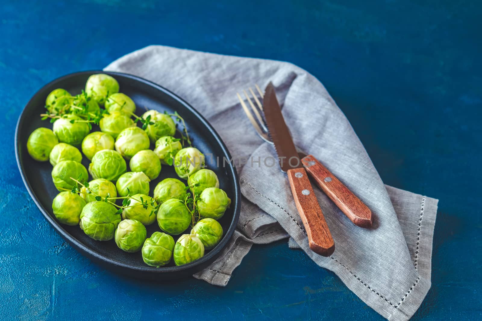 Fresh organic Brussels sprouts in served on black plate, dark blue concrete table surface, copy space for you text.