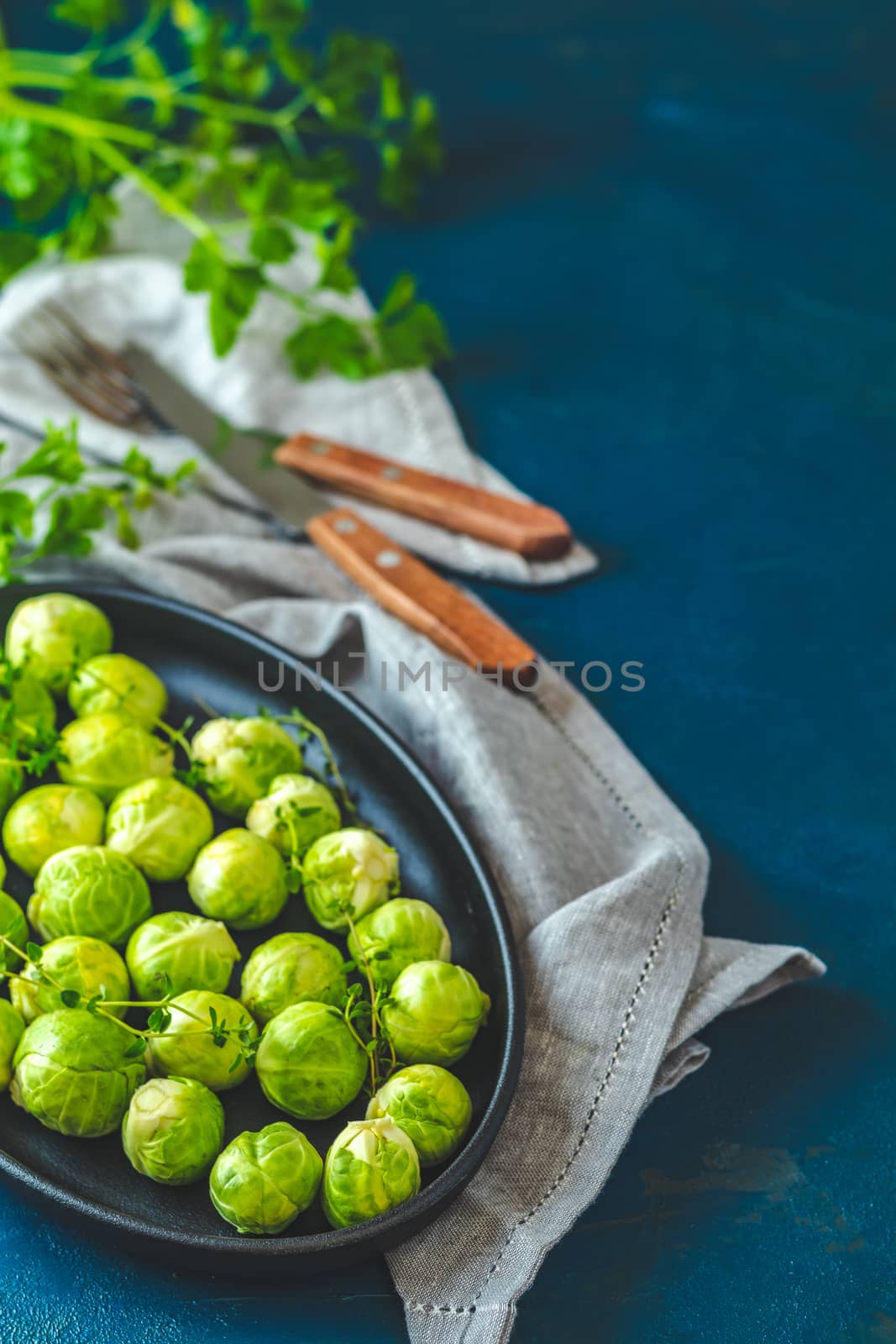 Fresh organic Brussels sprouts in served on black plate, dark blue concrete table surface, copy space for you text.