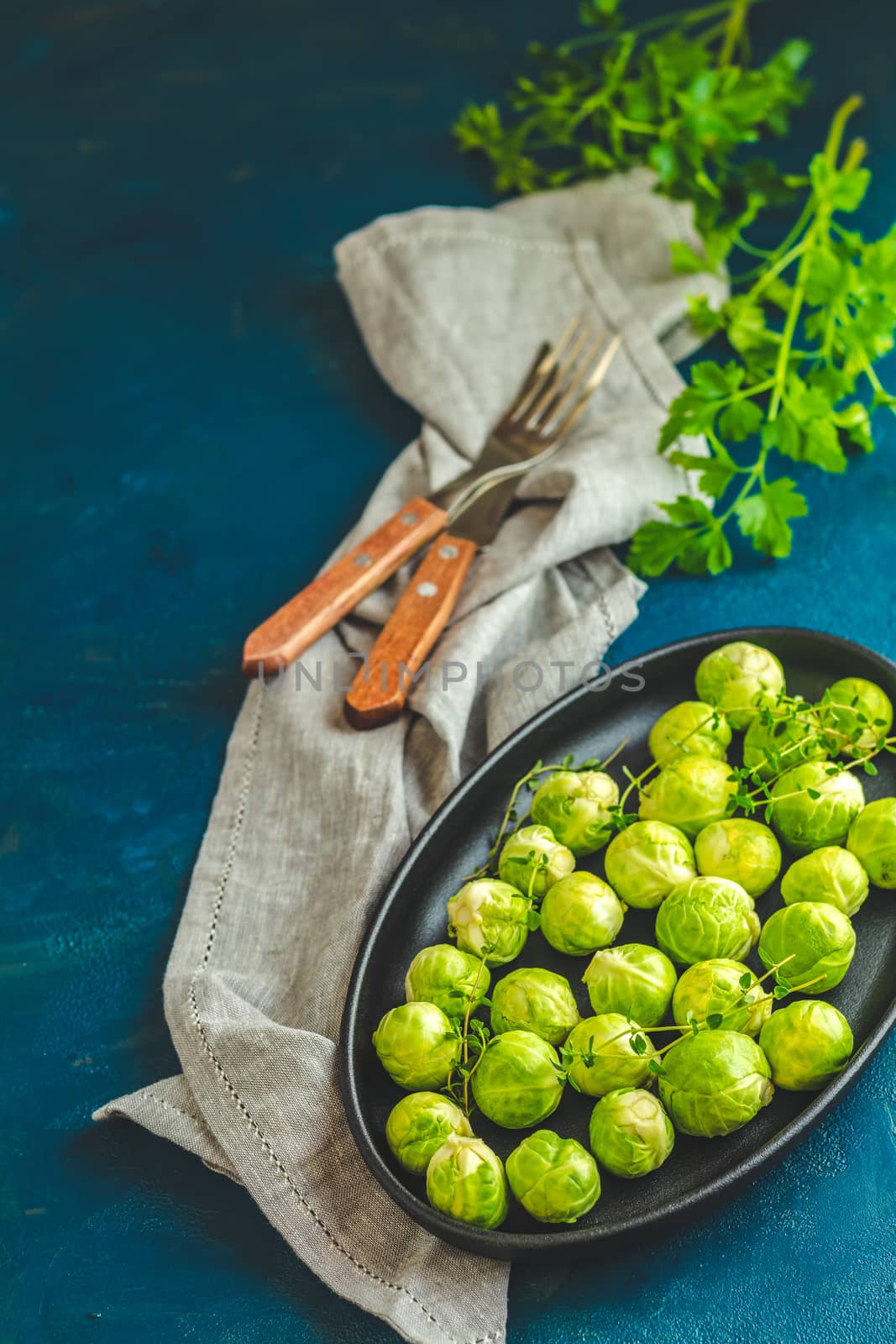 Fresh organic Brussels sprouts in served on black plate, dark blue concrete table surface, copy space for you text.