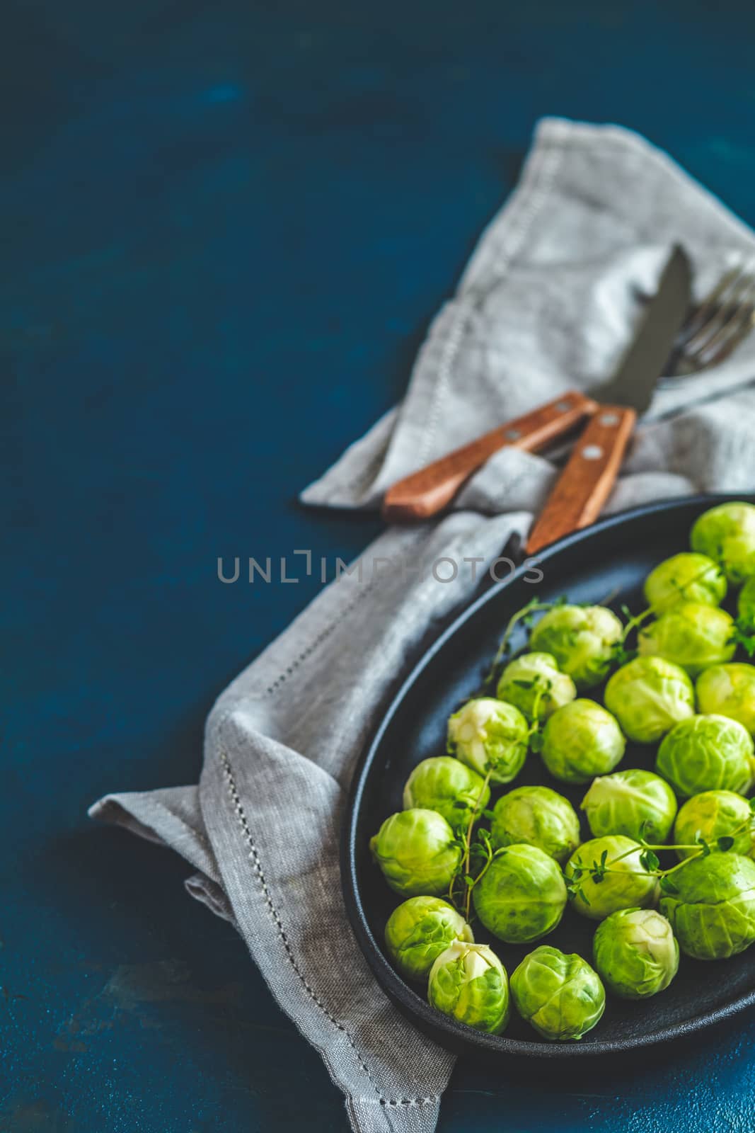 Fresh organic Brussels sprouts in served on black plate, dark blue concrete table surface, copy space for you text.