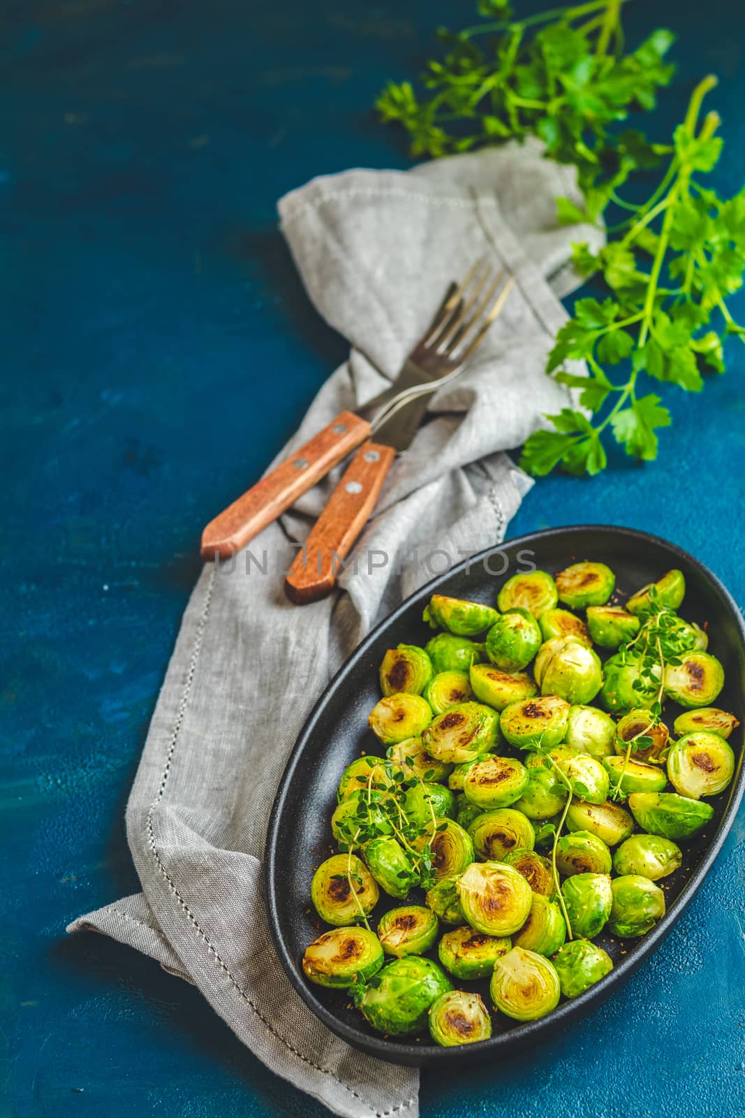 Black plate with delicious roasted Brussels sprouts in served on black plate, dark blue concrete table surface, copy space for you text.