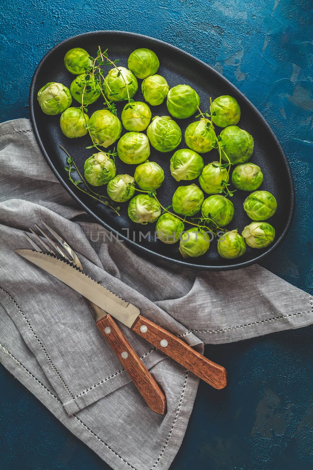 Fresh organic Brussels sprouts in served on black plate, dark blue concrete table surface, copy space for you text.