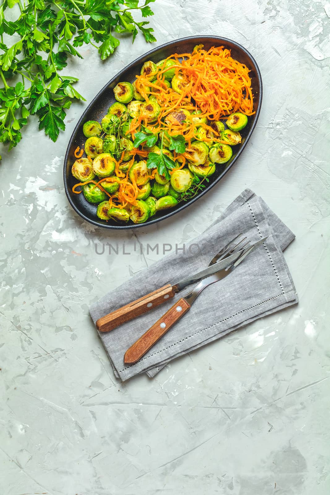 Delicious roasted Brussels sprouts and marinated carrot chips in served on black plate, light gray concrete table surface, top view, copy space for you text.