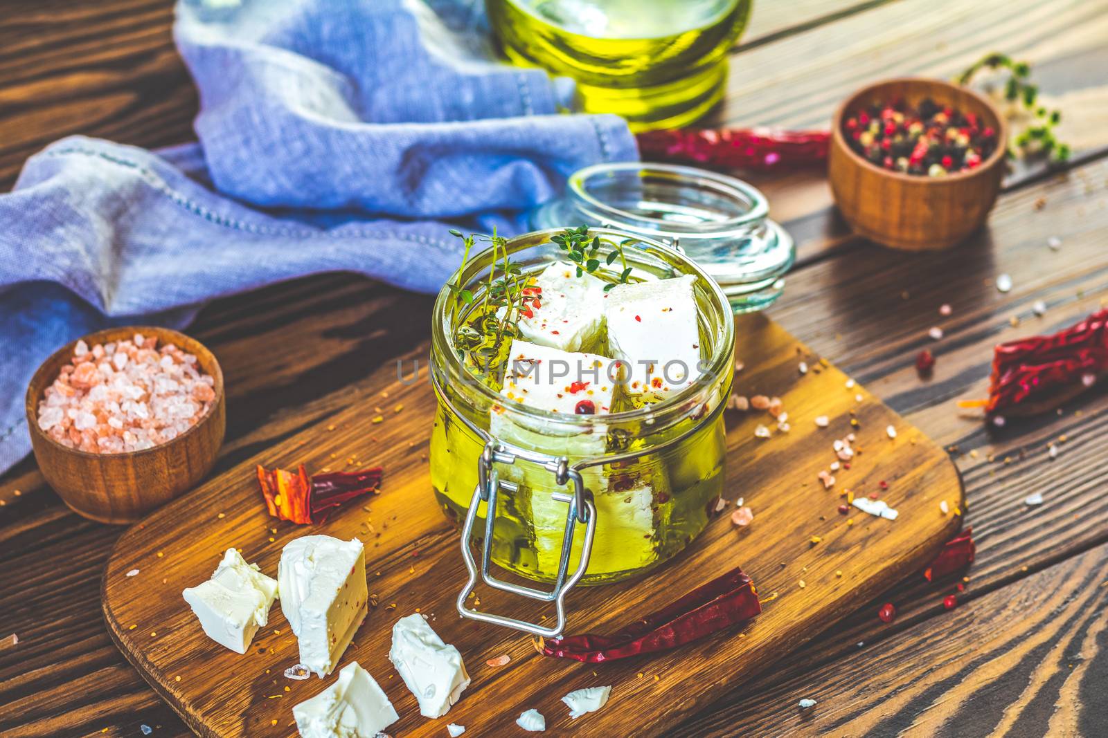 Feta cheese marinated in olive oil with fresh herbs in glass jar. Wooden background.