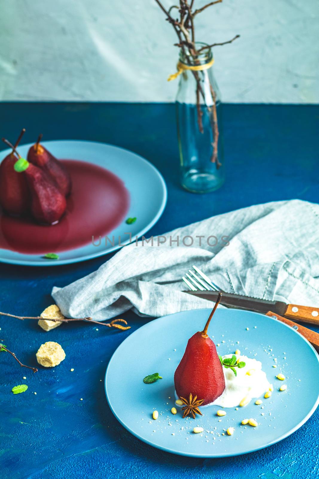Pears in wine. Traditional dessert pears stewed in red wine with chocolate sauce on plate on blue concrete surface. Concept for romantic dinner dessert. Simple Paleo style dessert pear