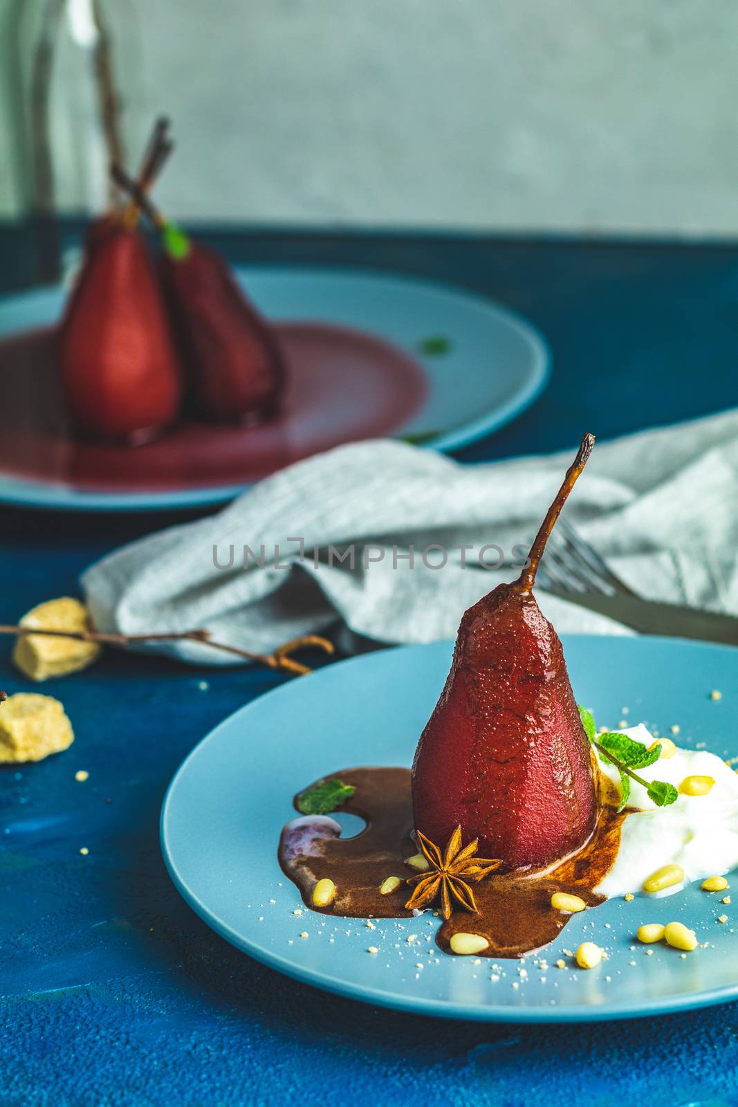 Pears in wine. Traditional dessert pears stewed in red wine with chocolate sauce on plate on blue concrete surface. Concept for romantic dinner dessert