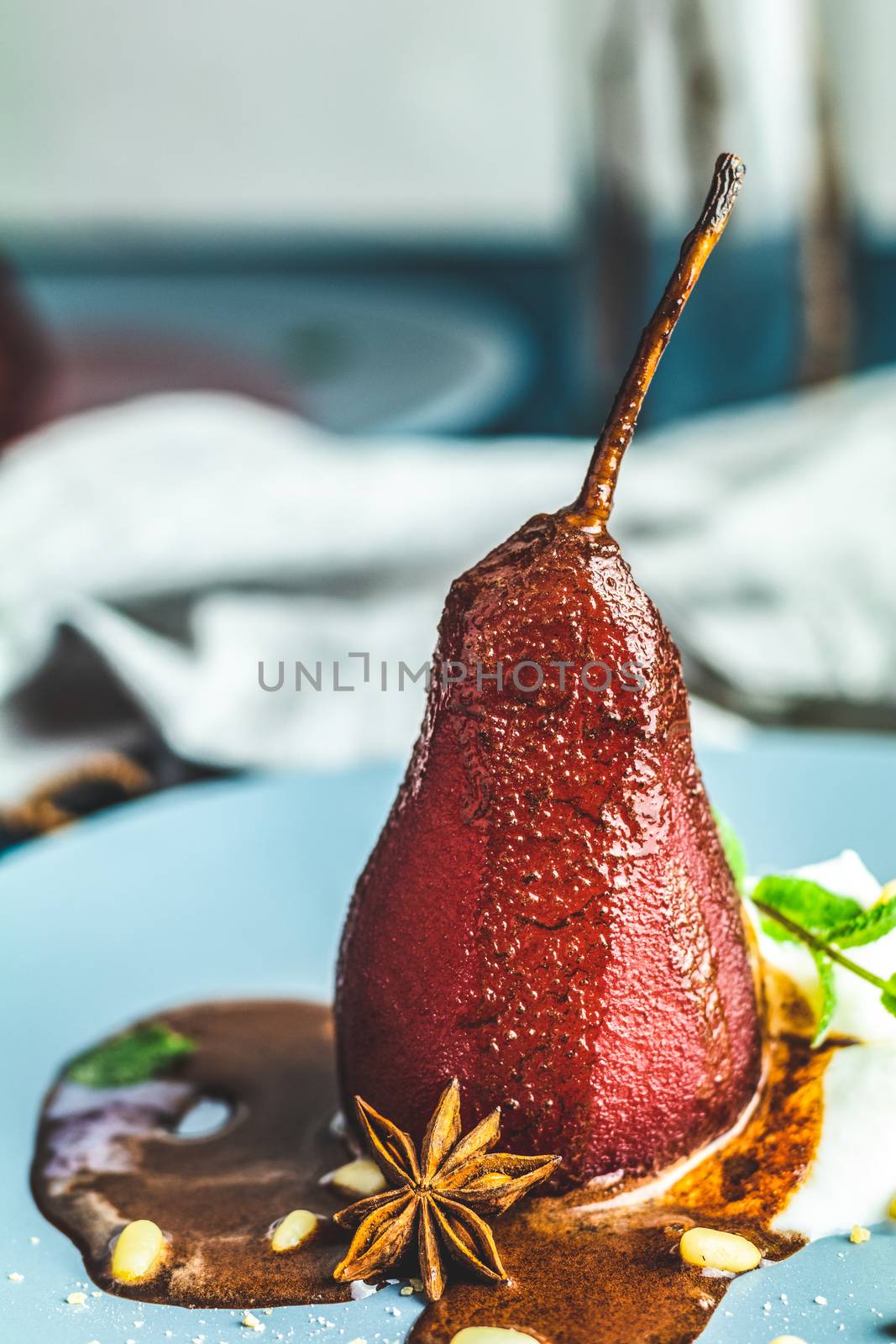 Pears in wine. Traditional dessert pears stewed in red wine with chocolate sauce on plate on blue concrete surface. Concept for romantic dinner dessert