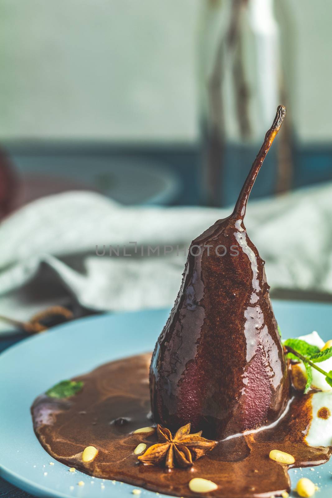 Pears in wine. Traditional dessert pears stewed in red wine with chocolate sauce on plate on blue concrete surface. Concept for romantic dinner dessert