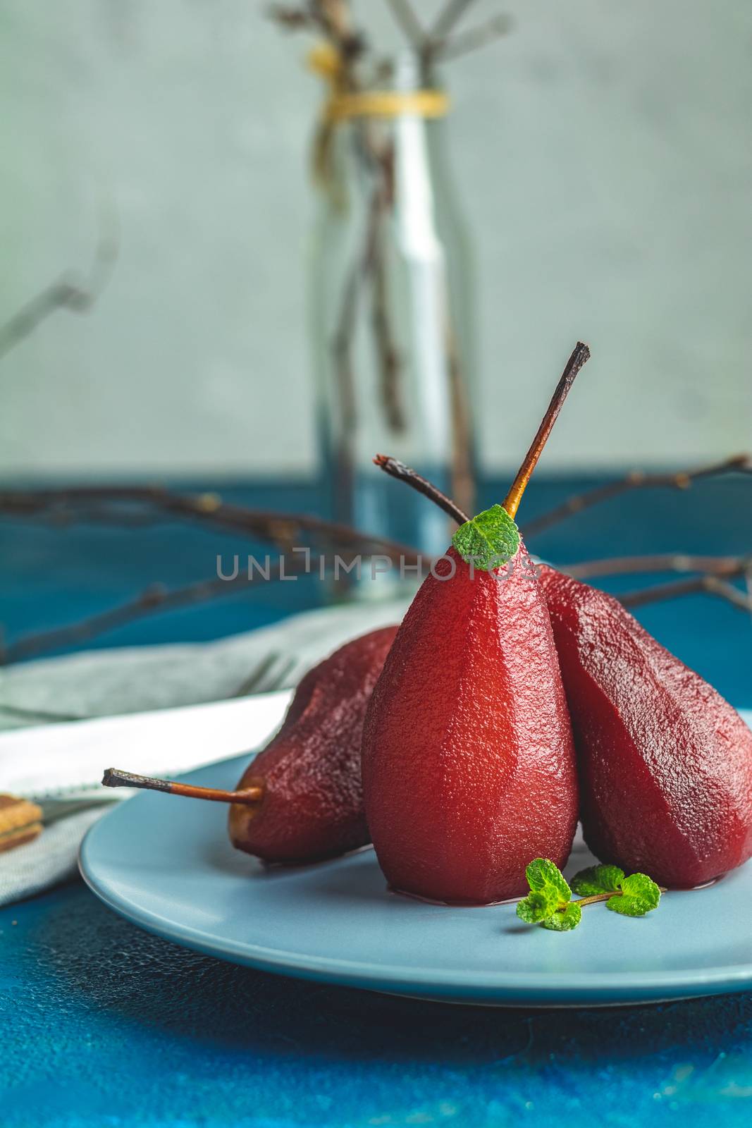 Traditional dessert pears stewed in red wine with chocolate sauce on plate on blue concrete surface. Concept for romantic dinner dessert. Simple Paleo style dessert pear poached in pomegranate juice