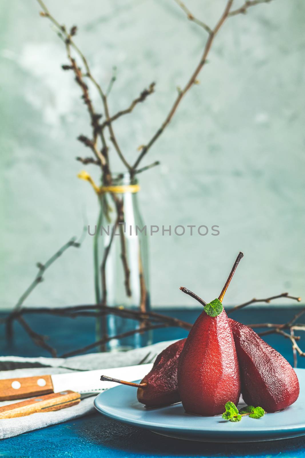 Traditional dessert pears stewed in red wine with chocolate sauce on plate on blue concrete surface. Concept for romantic dinner dessert. Simple Paleo style dessert pear poached in pomegranate juice
