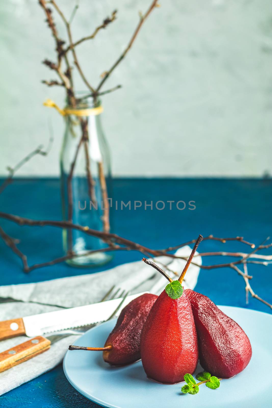 Pears in wine. Traditional dessert pears stewed in red wine with chocolate sauce on plate on blue concrete surface. Concept for romantic dinner dessert. Simple Paleo style dessert pear