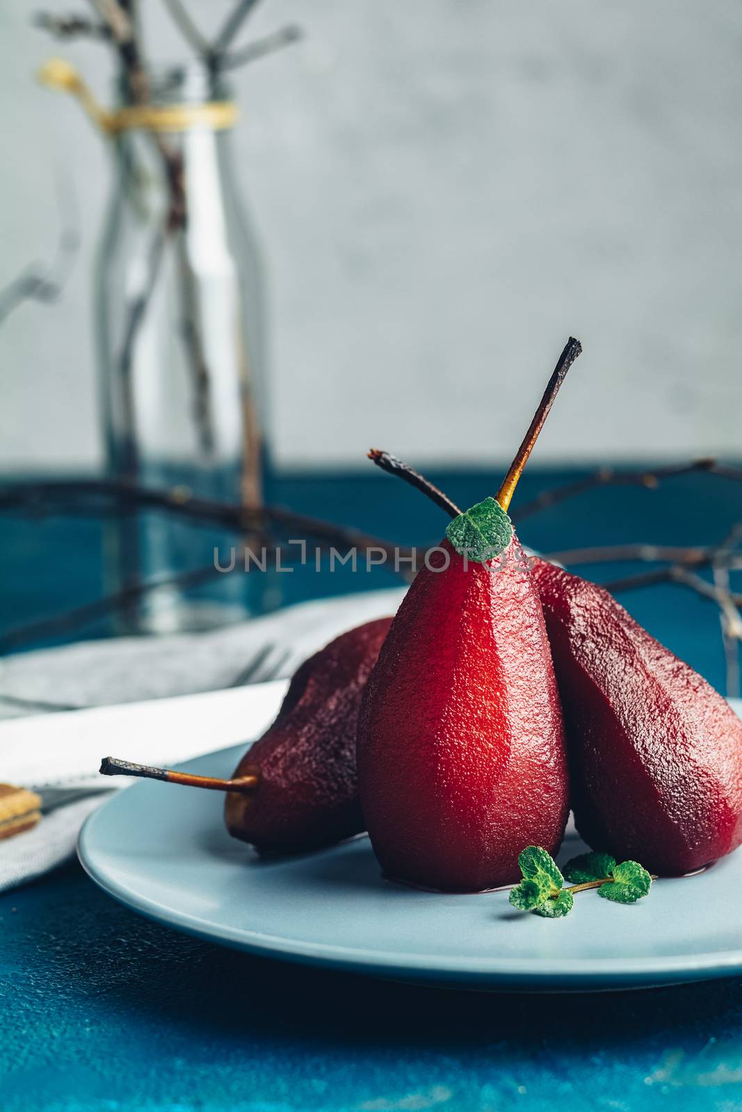 Pears in wine. Traditional dessert pears stewed in red wine with chocolate sauce on plate on blue concrete surface. Concept for romantic dinner dessert. Simple Paleo style dessert pear poached in pomegranate juice.