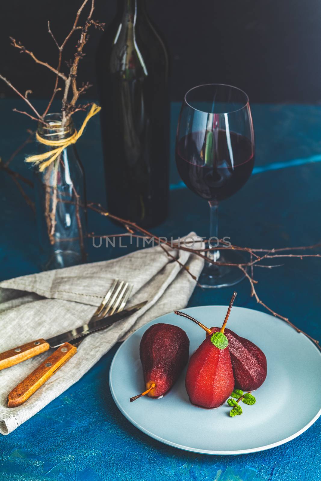 Pears in wine. Traditional dessert pears stewed in red wine with chocolate sauce on plate on blue concrete surface. Concept for romantic dinner dessert. Simple Paleo style dessert pear poached in pomegranate juice.