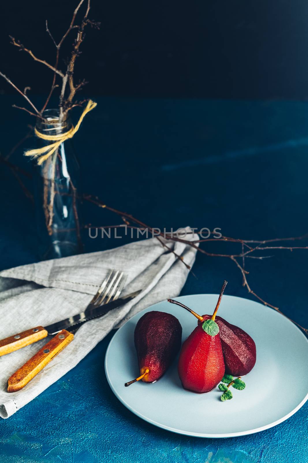 Pears in wine. Traditional dessert pears stewed in red wine with chocolate sauce on plate on blue concrete surface. Concept for romantic dinner dessert. Simple Paleo style dessert pear