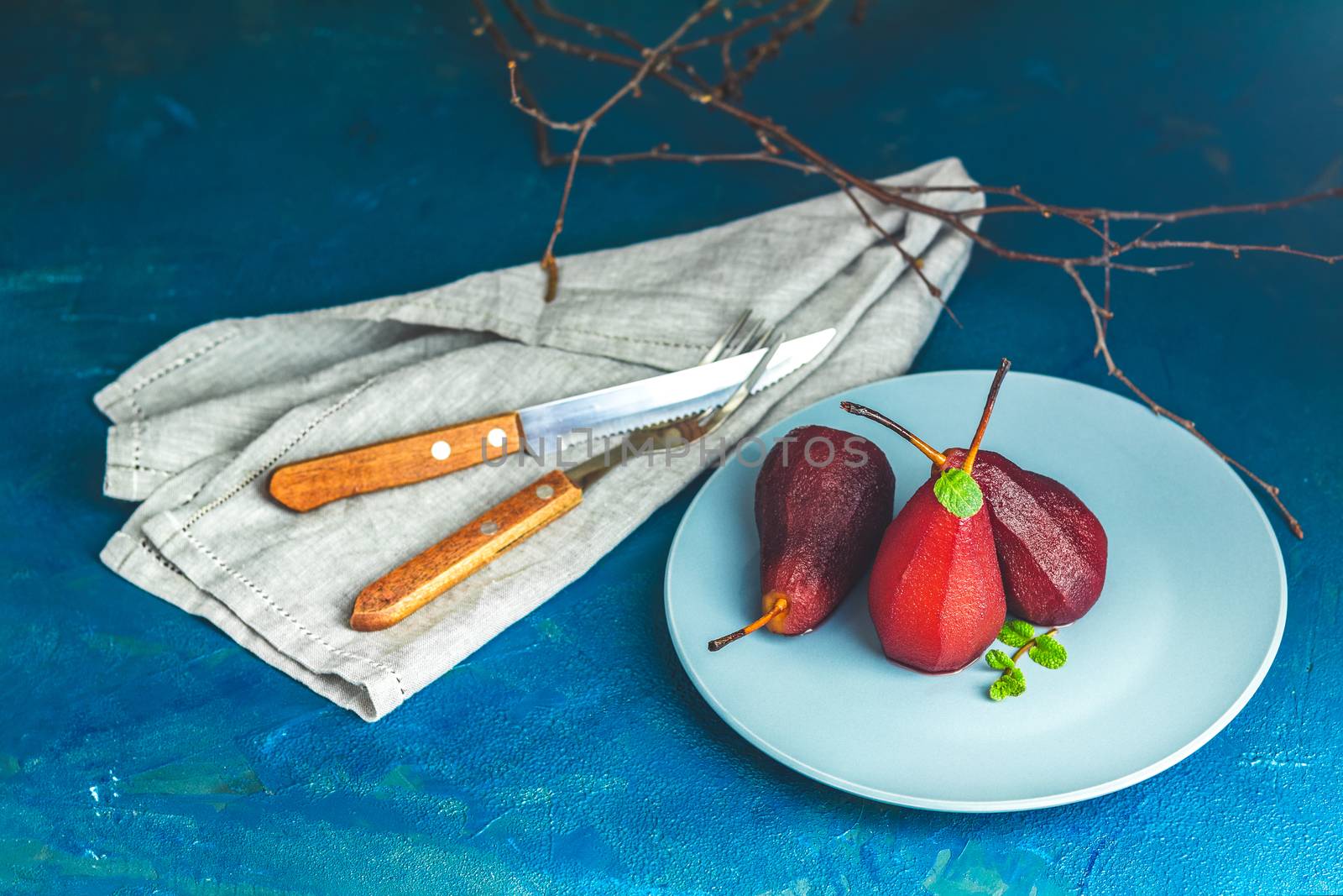 Pears in wine. Traditional dessert pears stewed in red wine with chocolate sauce on plate on blue concrete surface. Concept for romantic dinner dessert. Simple Paleo style dessert pear