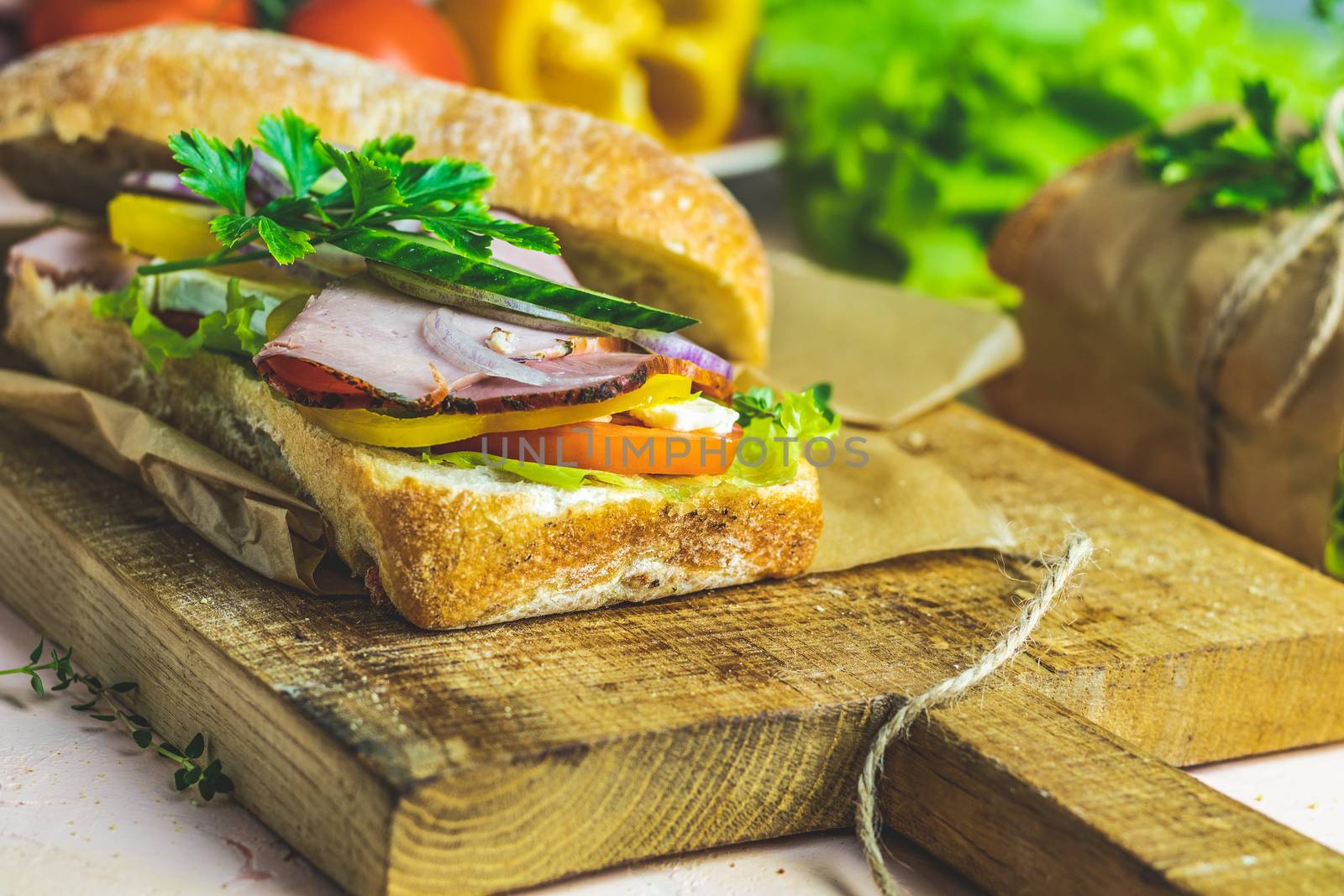 Italian porchetta sandwich. Ciabatta sandwich with ham, tomato, cheese, pepper, onion and salad on wooden cutting board with ingredients.