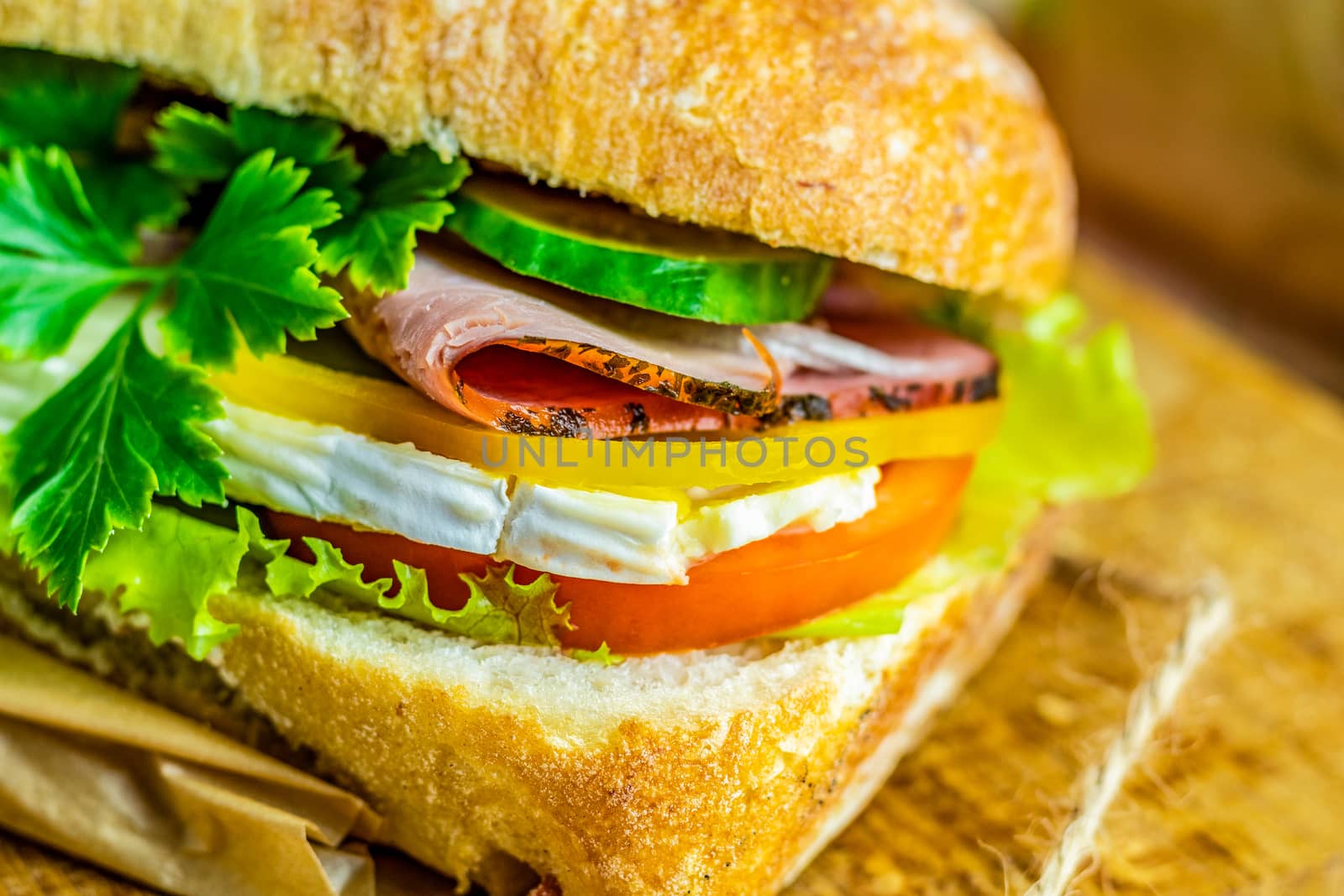 Italian porchetta sandwich. Ciabatta sandwich with ham, tomato, cheese, pepper, onion and salad on wooden cutting board with ingredients.