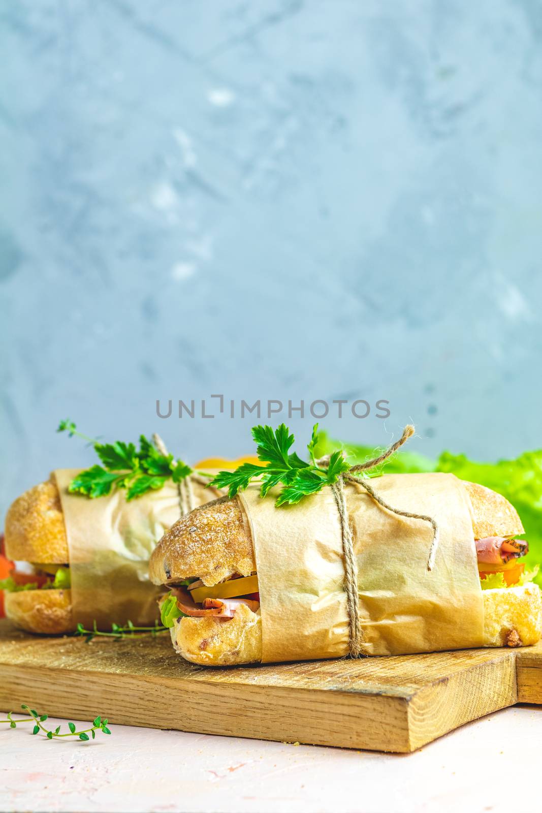 Ciabatta sandwich with ham, tomato, cheese, pepper, onion and salad on wooden cutting board with ingredients.