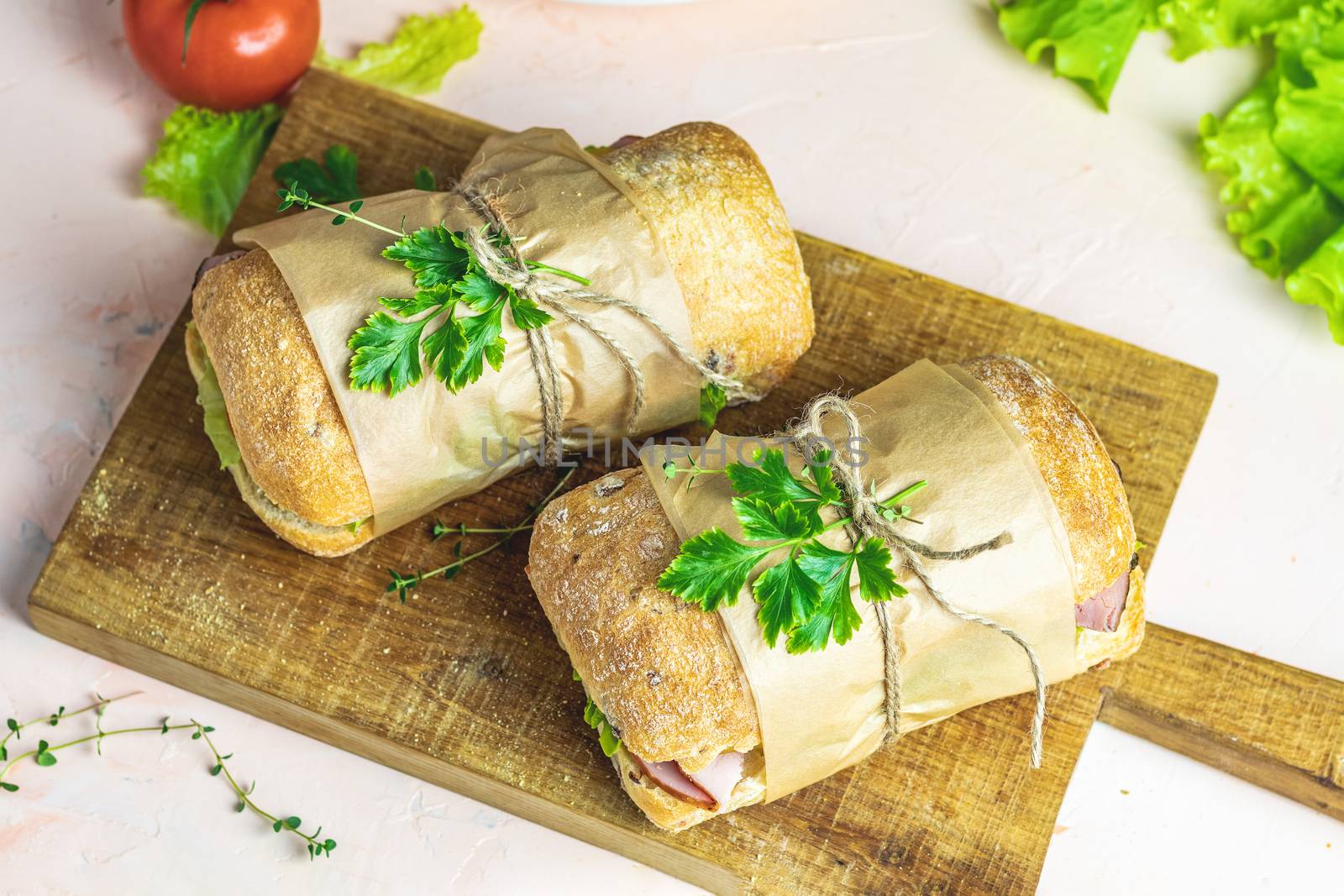 Italian porchetta sandwich. Ciabatta sandwich with ham, tomato, cheese, pepper, onion and salad on wooden cutting board with ingredients.