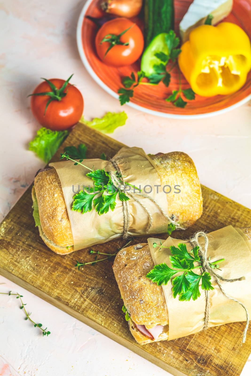 Ciabatta sandwich with ham, tomato, cheese, pepper, onion and salad on wooden cutting board with ingredients.